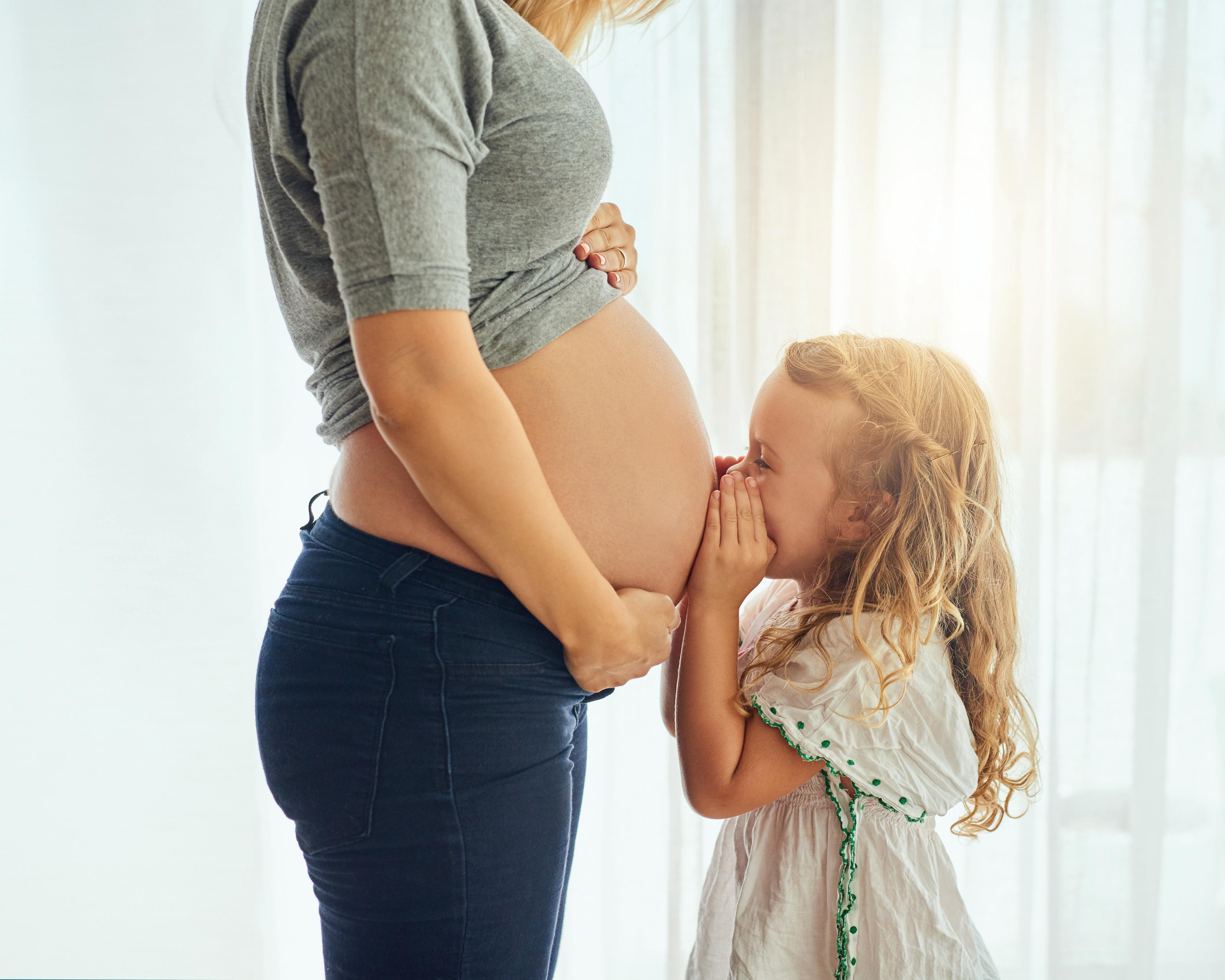 Little girl kissing mums pregnant tummy